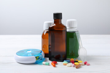 Bottles of syrup, dosing spoon and pills on white table against light grey background. Cold medicine