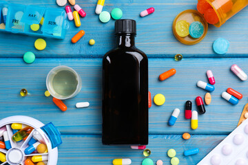 Flat lay composition with bottle of syrup, measuring cup and pills on light blue wooden table. Cold...
