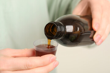 Woman pouring syrup from bottle into measuring cup, closeup. Cold medicine
