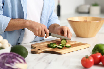 Man cutting cucumber at table in kitchen, closeup. Online cooking course