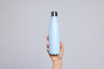 Woman holding thermo bottle on light grey background, closeup