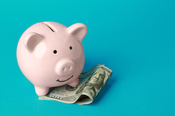 Ceramic piggy bank and banknotes on turquoise background. Space for text