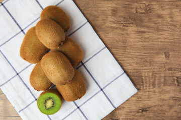 Heap of whole and cut fresh kiwis on wooden table, top view. Space for text