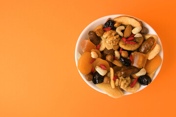 Bowl with mixed dried fruits and nuts on orange background, top view. Space for text