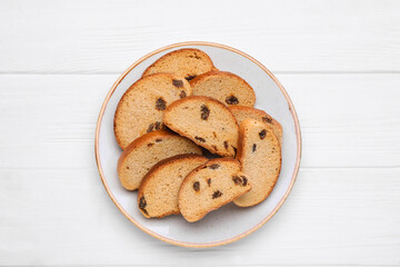 Plate of sweet hard chuck crackers with raisins on white wooden table, top view