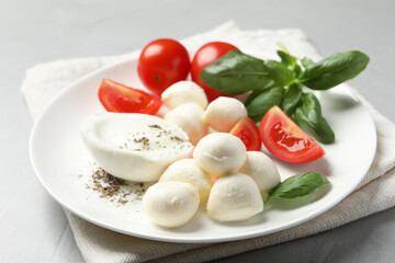 Delicious mozzarella with tomatoes and basil leaves on light gray table