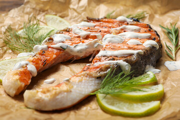 Tasty salmon steak with sauce, citrus slices and dill on parchment paper, closeup