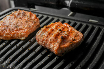 Tasty salmon cooking on electric grill, closeup