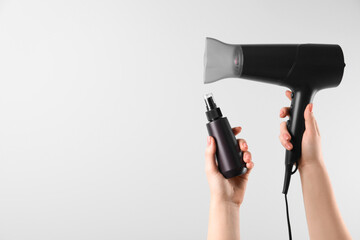Woman holding spray bottle with thermal protection and hairdryer on white background, closeup....