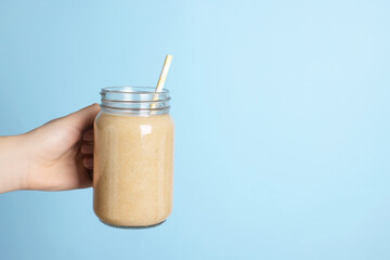 Woman holding mason jar with tasty smoothie and straw on light blue background, closeup. Space for...