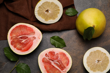 Fresh cut and whole pomelo fruits with green leaves on dark table, flat lay
