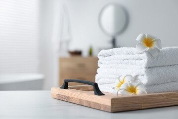 Fototapeta na wymiar Wooden tray with stacked bath towels and beautiful flowers on white table in bathroom. Space for text
