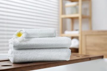 Fototapeta na wymiar Stacked bath towels and beautiful flower on tub tray in bathroom. Space for text