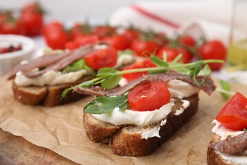 Delicious bruschettas with anchovies, tomatoes, microgreens and cream cheese on wooden board,...