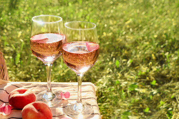 Glasses of delicious rose wine with petals and peaches on white picnic blanket outside. Space for...