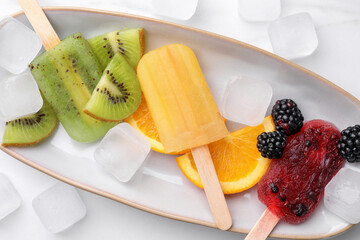Plate of delicious popsicles, ice cubes and fresh fruits on white background, top view