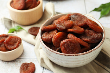 Tasty apricots in bowls on white tiled table, closeup. Dried fruits