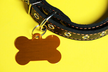 Black leather dog collar with golden tag in shape of bone on yellow background, closeup. Space for...