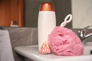 Pink sponge, seashell and shower gel bottle on washbasin in bathroom, closeup. Space for text