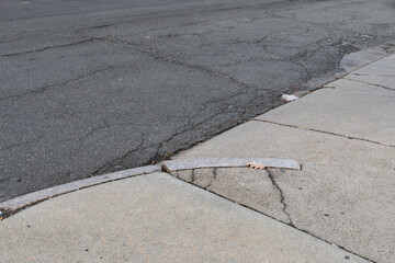 Cracked concrete driveway and curb leading into an asphalt street, transportation background,...