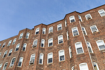 Oblique view of the undulating surface of a generic urban brick apartment building, view looking up at blue sky beyond, horizontal aspect