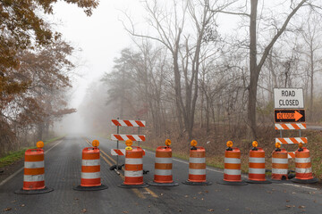 Straight road disappearing into a dense fog, barricade of bright orange traffic barrels, horizontal...