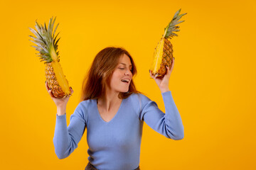Woman with a pineapple in sunglasses, dancing and happy with the pineapple cut in half, yellow background