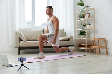 Man sports, watching a workout tape on his phone and repeating exercises sports blogger with dumbbells, pumped up man fitness trainer works out at home, the concept of health and body beauty