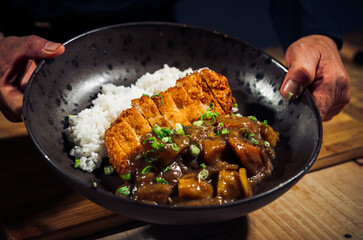 Japanese chicken katsu curry rice, deep fried breast chicken fillet with beef, carrot and potato curry in black plate on wooden table Crispy fried pork cutlet with curry rice  - Japanese food style