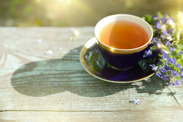 Cup of tea and blue flowers bouquet on wooden table on a terrace in summer morning. Herbal Tea, wildflowers and herbs on a blurred background, soft focus