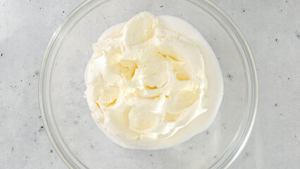Cream cheese and sugar in a bowl. Cheesecake recipe, mixing ingredients in a glass bowl, close-up view from above