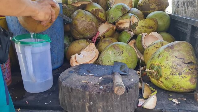 close-up of the hands of an Indonesian iced coconut seller cutting coconuts using a large knife. Street fruit seller's hands peel fresh green coconuts with the help of a cutting knife
