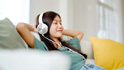 Young asian woman listening to music on couch in living room at home. Happy asia female using...