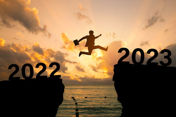 2023 new year concept, new year card.Silhouette of a businessman jumping on a cliff in 2023 over...