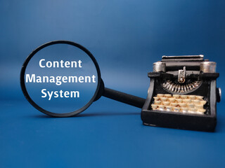 Magnifying glass and vintage type writter with the word Content Management System on blue...