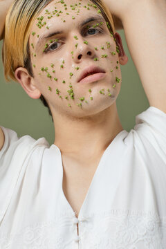 Low angle view portrait of feminine guy posing with beauty mask and tiny green flowers on his face