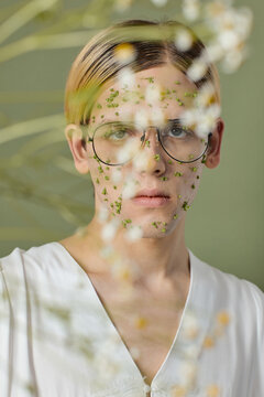 Young male model with face mask wearing glasses standing behind flowers