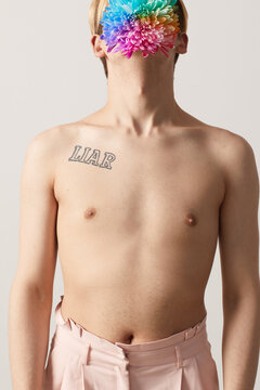 Topless young man with amazing rainbow dahlia in mouth hiding his face