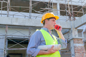 Naklejka na ściany i meble American man technician Industrial engineer using walkie-talkie and holding blueprint working in construction site for building site survey in civil engineering project.