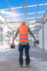 Male engineer wearing safety suit and hard hat holding toolbox and electric drill in construction site for building site survey in civil engineering project.