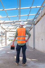 Male engineer wearing safety suit and hard hat holding toolbox and electric drill in construction site for building site survey in civil engineering project.