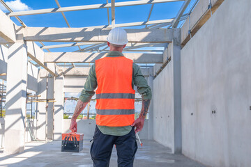 Male engineer wearing safety suit and hard hat holding toolbox and electric drill in construction site for building site survey in civil engineering project.