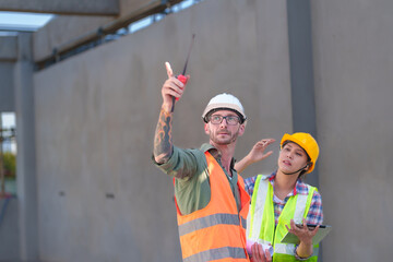 Two professionals inspect construction site of commercial building, industrial building, real estate project  civil engineer, investor using laplet in background crane, skyscraper, concrete formwork