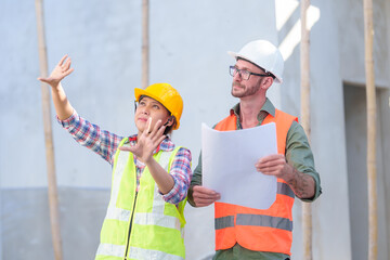 Two professionals inspect construction site of commercial building, industrial building, real estate project  civil engineer, investor using laplet in background crane, skyscraper, concrete formwork