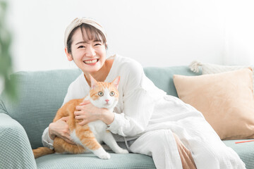 家のソファで猫を抱っこする飼い主のアジア人女性
