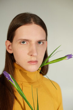 Pretty gender neutral model wearing red turtleneck sweater and white pants while standing on gray background and looking at camera