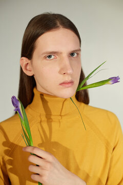 Handsome androgynous man with lovely small flowers looking at camera with serious face expression