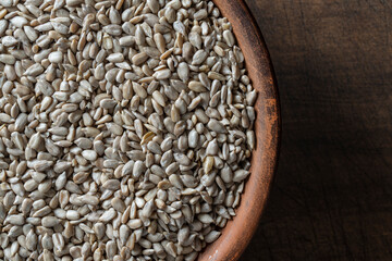Grey raw sunflower seeds in ceramic bowl on a wooden background, closeup, top view. Purified seeds of sunflower