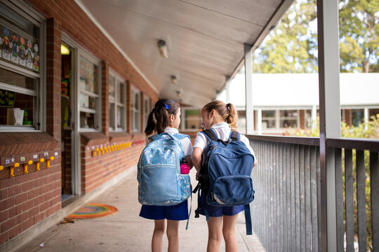 Two young schoolgirls walking along outdoor hallway at school