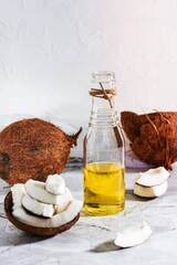Fototapeta na wymiar Fresh vegetable coconut oil in a bottle and pieces of coconut on the table. Vertical view